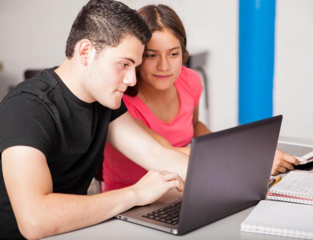 Using a laptop together at school Couple of Hispanic teenagers stuying and using a laptop together at school